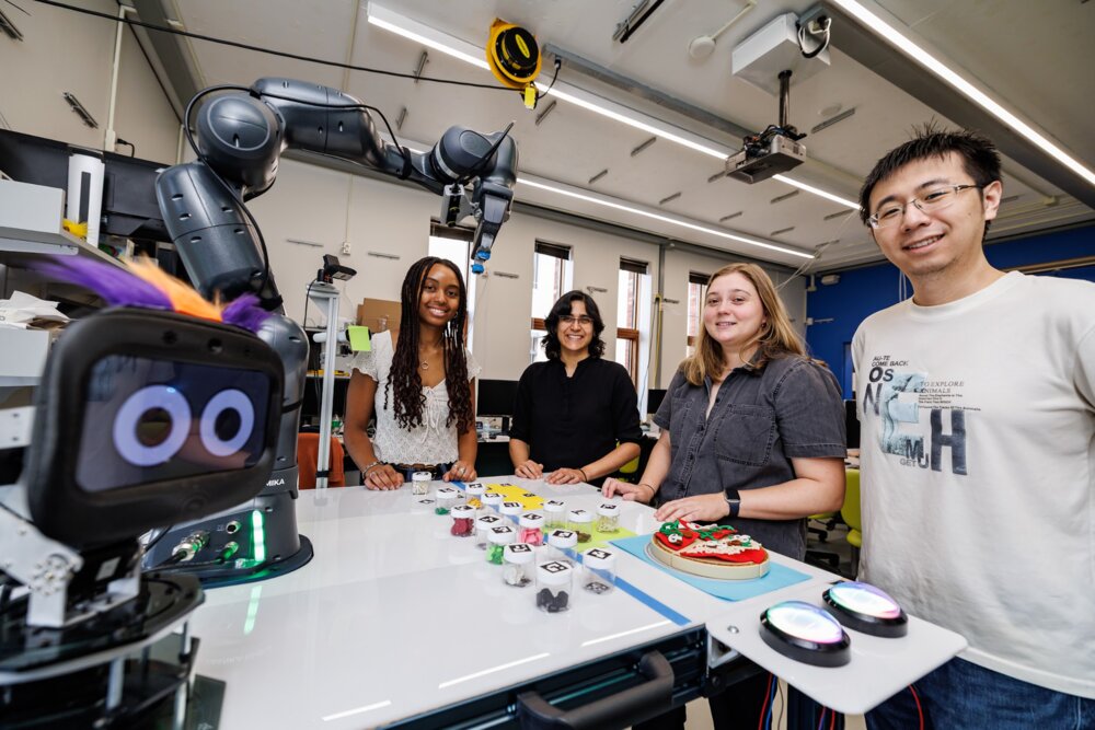 Alyssa Quarles, Marynel Vazquez, Kate Candon, and Qiping Zhang pose around a robot arm and preference-learning setup in a lab.