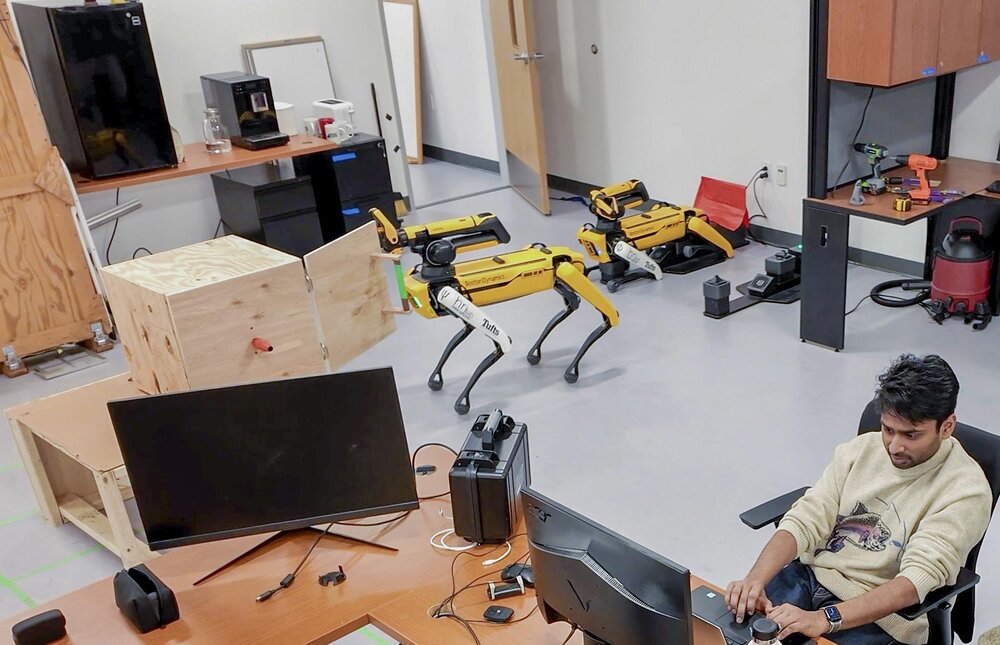 Graduate student Shivam Goel at a computer monitoring two Spot robots in a Tufts lab.