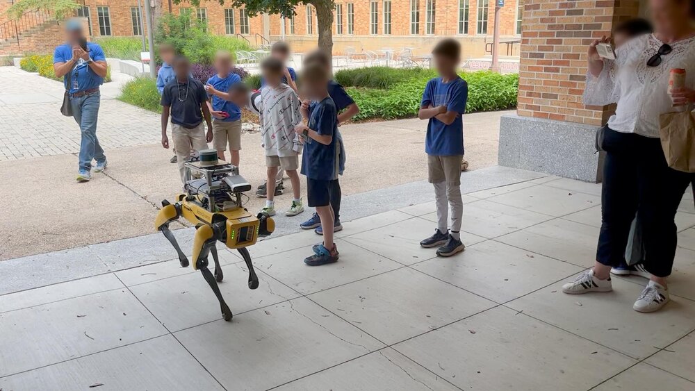 A Spot robot leads a group of students on a tour outside a UT Austin building.